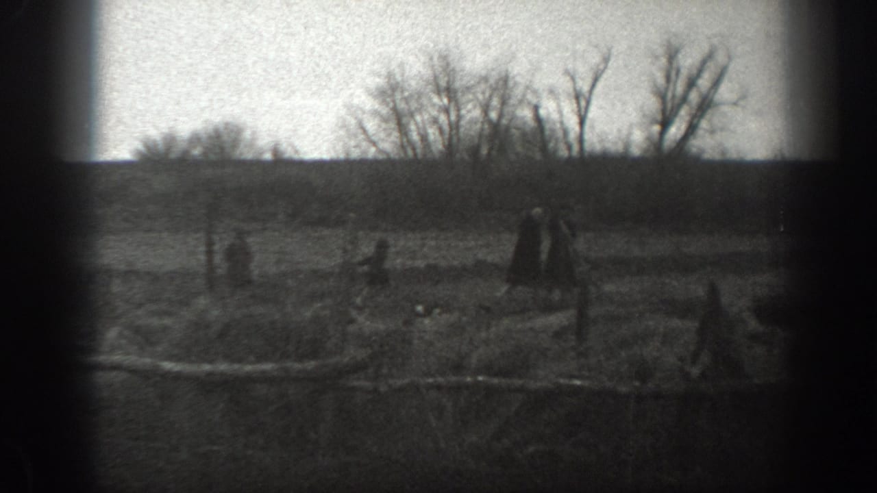1939 Montana 8mm frame showing distant people in an open rural field with fence posts, bare trees and a low horizon.