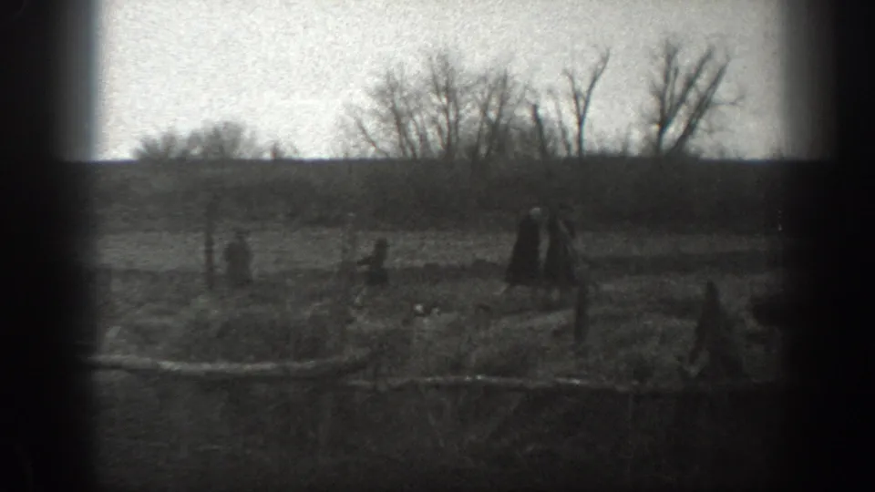 1939 Montana 8mm frame showing distant people in an open rural field with fence posts, bare trees and a low horizon.
