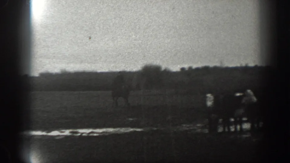 In 1939 Montana home-movie footage, a distant man on horseback moves across a wet rural field beneath a pale sky.