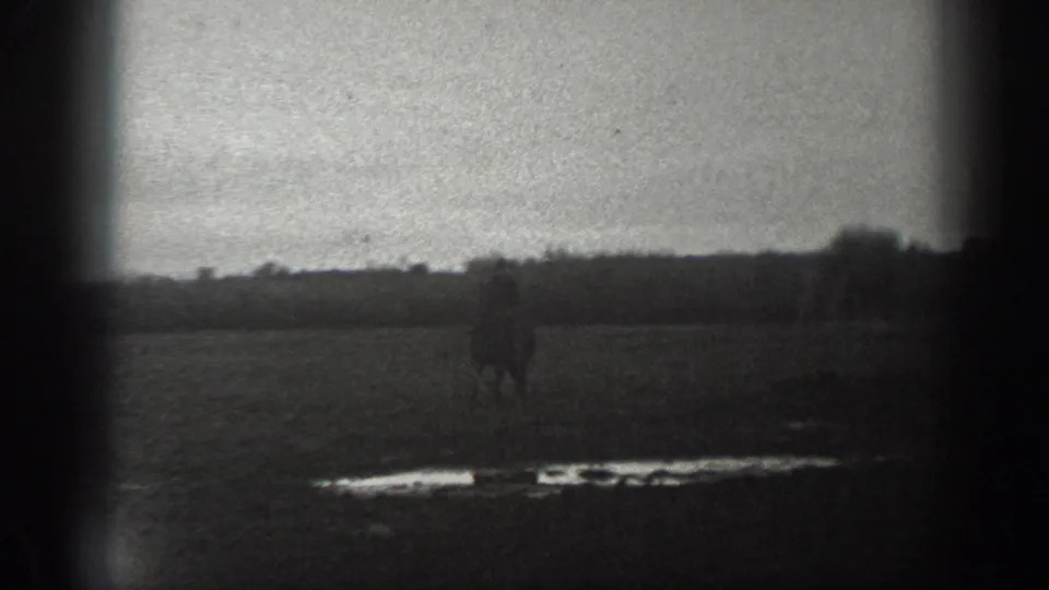 The rider continues across the rural Montana field, partly silhouetted against the soft horizon and grainy sky.