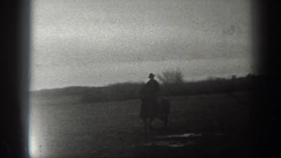 The mounted man is seen closer in profile within the rural Montana landscape, with puddled ground and a low distant horizon.