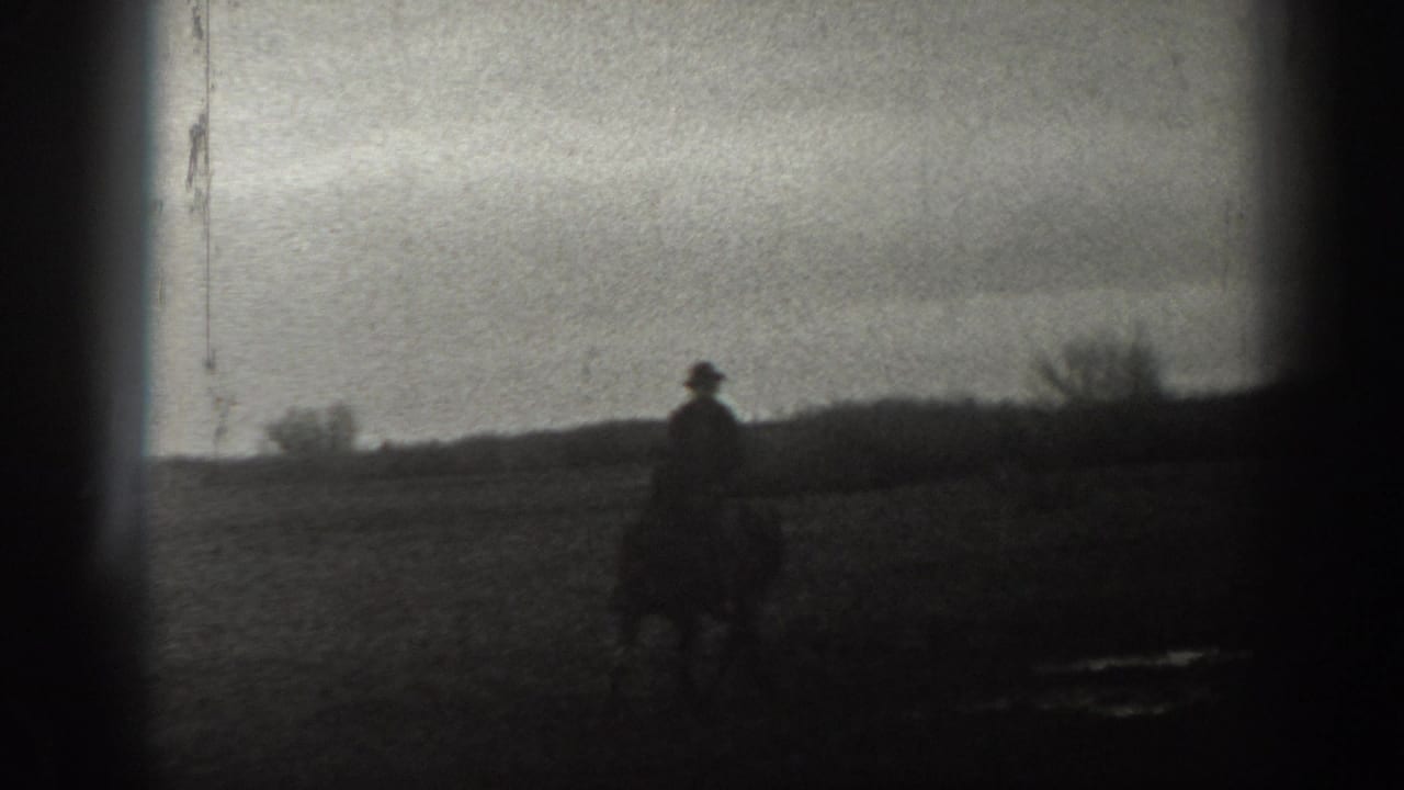 A dark, soft-focused 8mm frame shows a silhouetted person outdoors against a pale sky and low horizon, likely from the same Montana home movie.