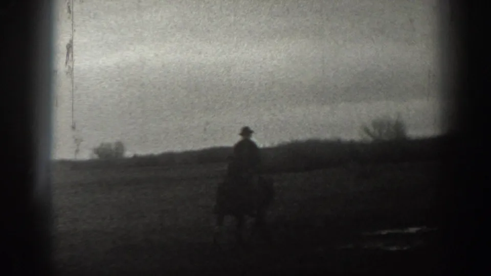 A dark, soft-focused 8mm frame shows a silhouetted person outdoors against a pale sky and low horizon, likely from the same Montana home movie.