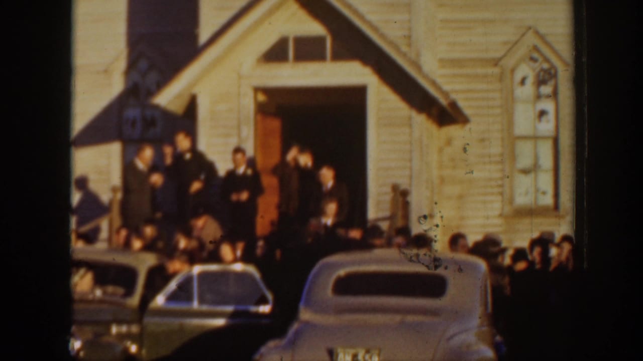 1939 Montana wedding guests stand near a wood-sided church entrance while rounded classic cars fill the foreground.