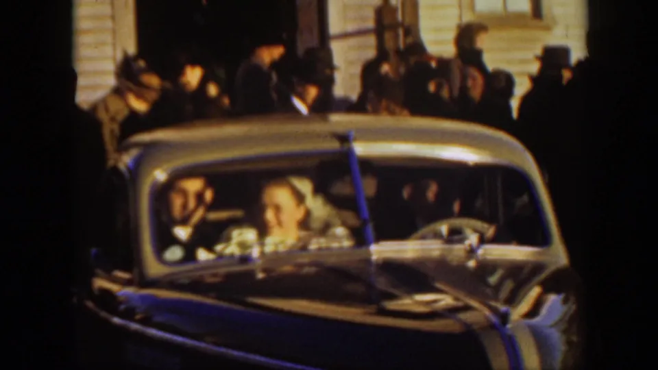 The bride and groom appear in a decorated classic car outside the Montana church, with wedding guests gathered behind them.