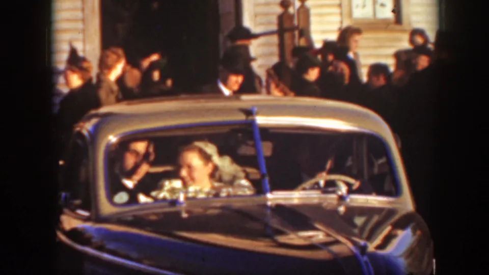 Close 8mm view of the bride and groom seated in a decorated car outside the 1939 Montana wedding gathering.