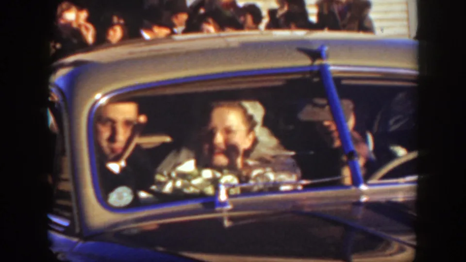 A close view through the car windshield shows the bride, groom, and driver during the Montana wedding departure, with guests partly visible behind.