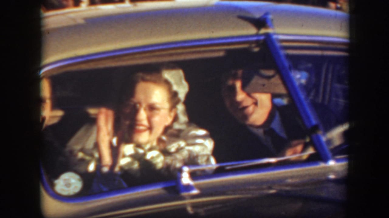 1939 Montana home-movie frame showing a smiling bride in a car beside two men, with soft focus and warm 8mm color.