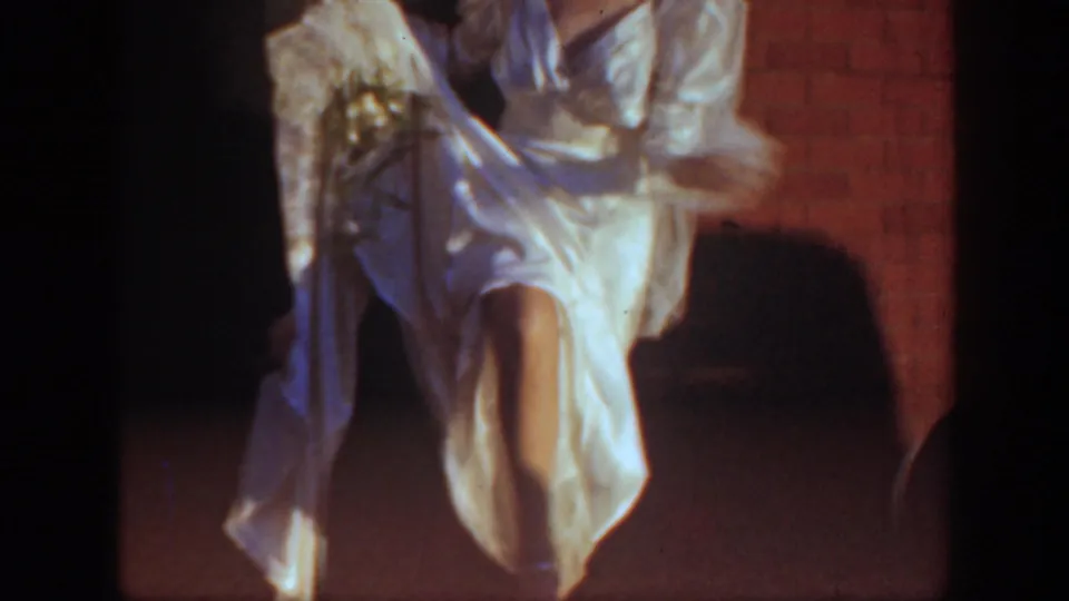 The bride lifts her white gown near the brick church wall, with one leg visible beneath the dress in a candid wedding moment.