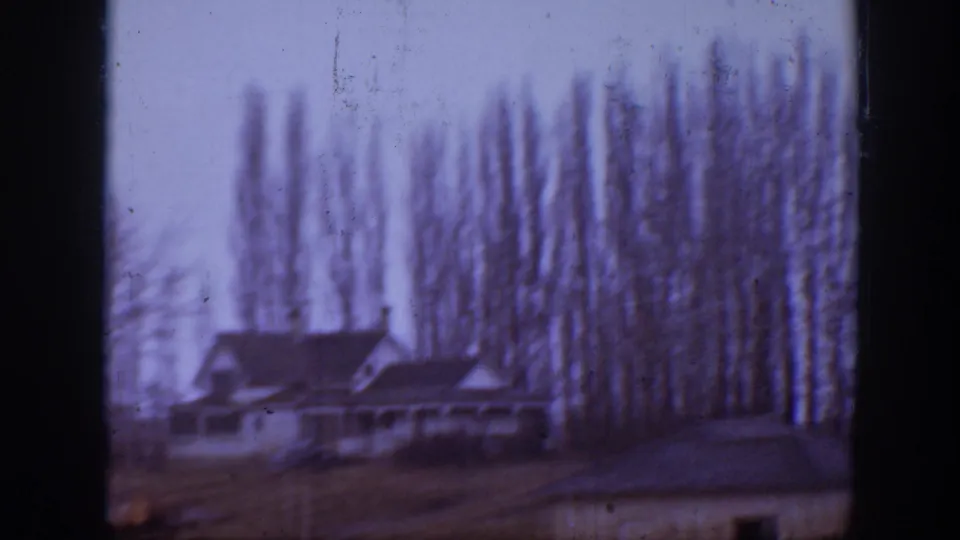 Rural Montana farmhouse appears behind tall trees in a faded 1939 8mm home-movie frame.