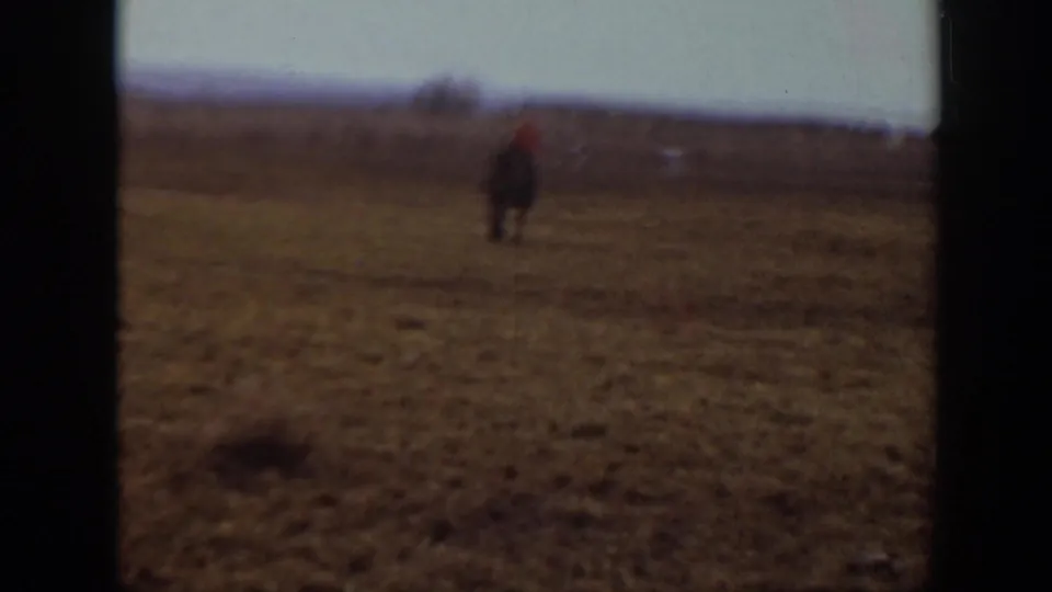 A small mounted figure continues across the open Montana prairie, with muted color and visible 8mm frame edges.