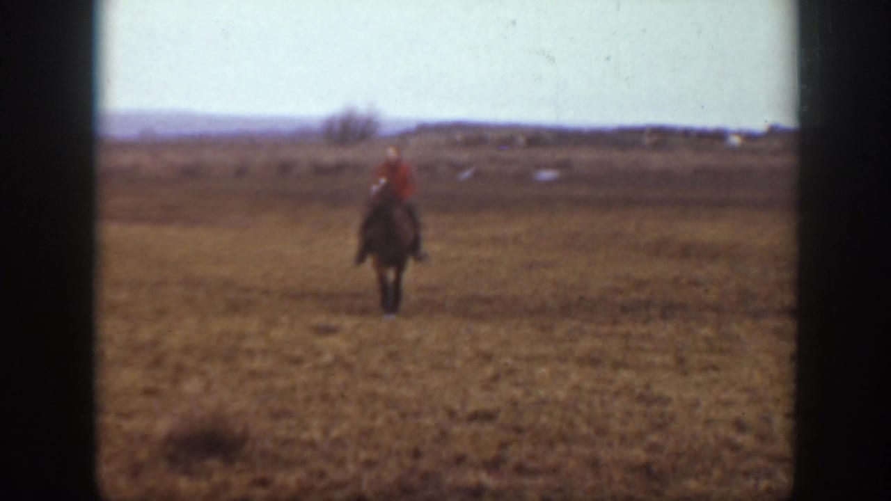 1939 Montana home-movie frame with a red-shirted rider on horseback crossing open grassland.