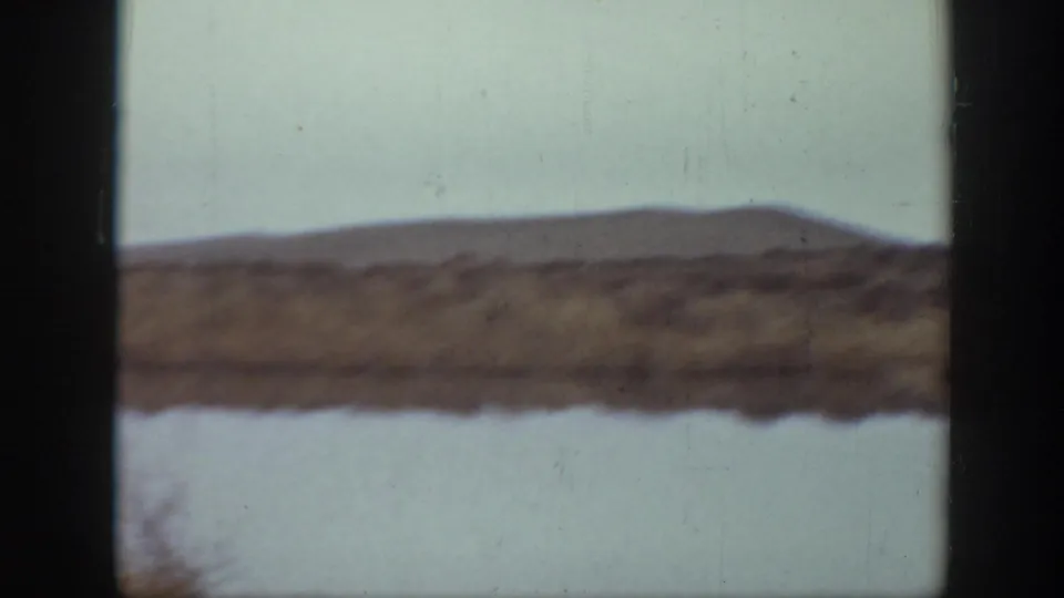 1939 Montana 8mm frame showing water, scrubby shoreline, and low hills with no clear people visible.