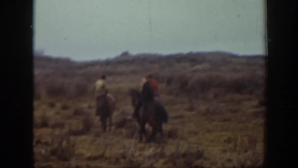 1939 Montana home-movie frame showing three riders on horseback moving through dry terrain near low hills.