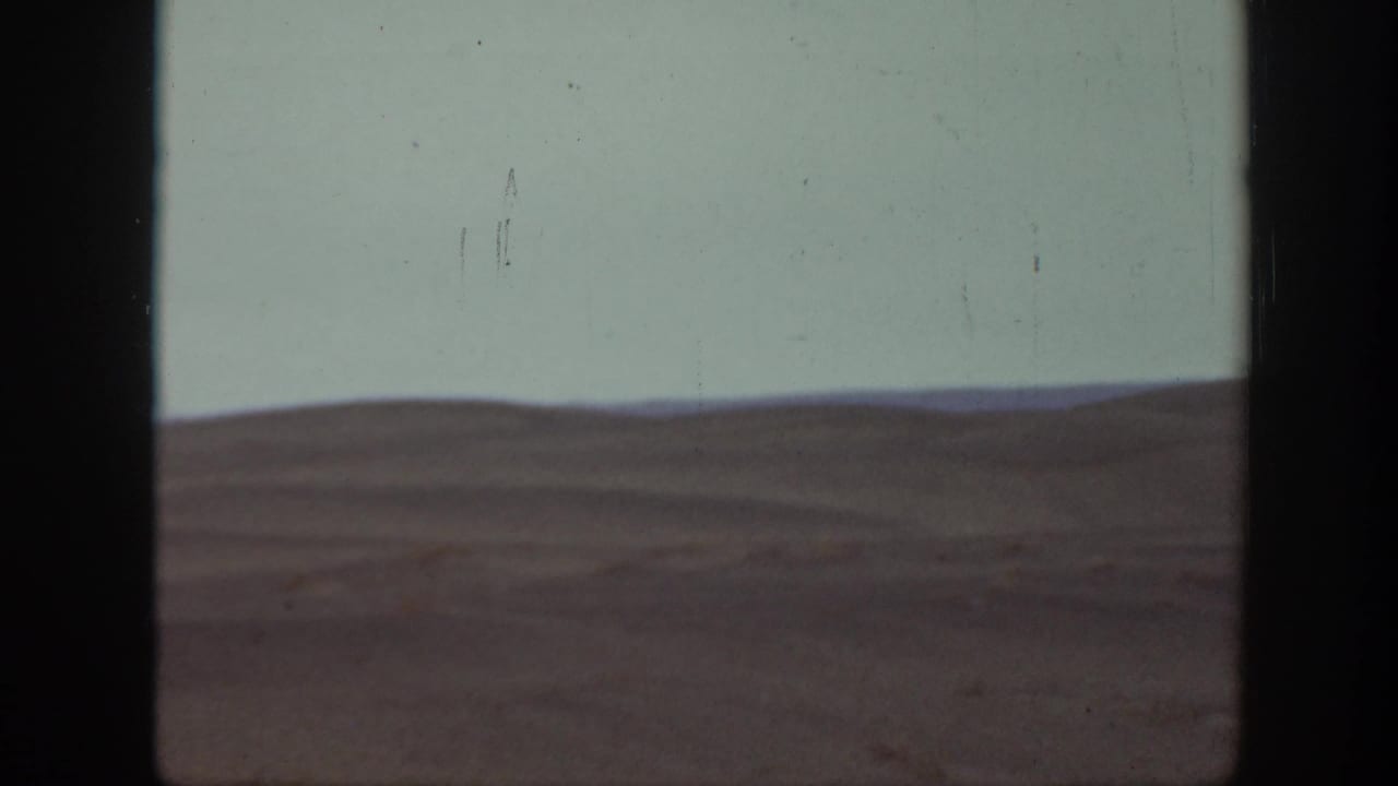 Wide open landscape with low hills and pale sky, framed by dark film edges.