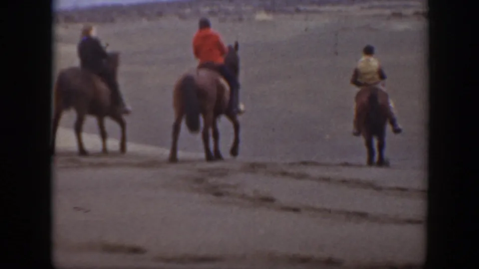 In the 1939 Montana scene, two mounted riders and a nearby person on foot pause or turn on open sandy terrain, with another rider at the edge.