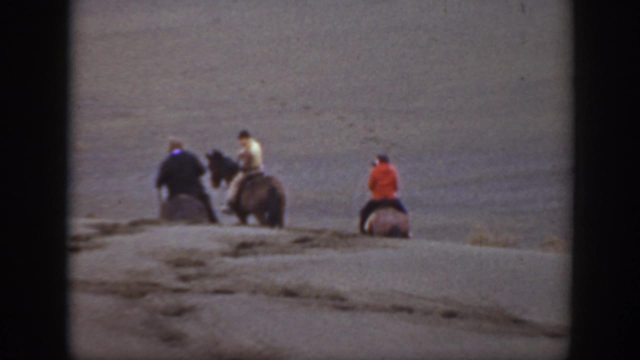 Four horseback riders appear farther away on a low rise in open terrain.