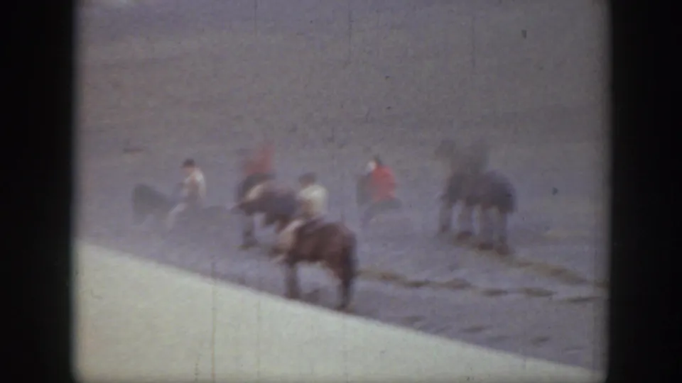 Soft, blurred 8mm frame of horseback riders crossing open Montana ground, with a pale foreground edge cutting into the view.