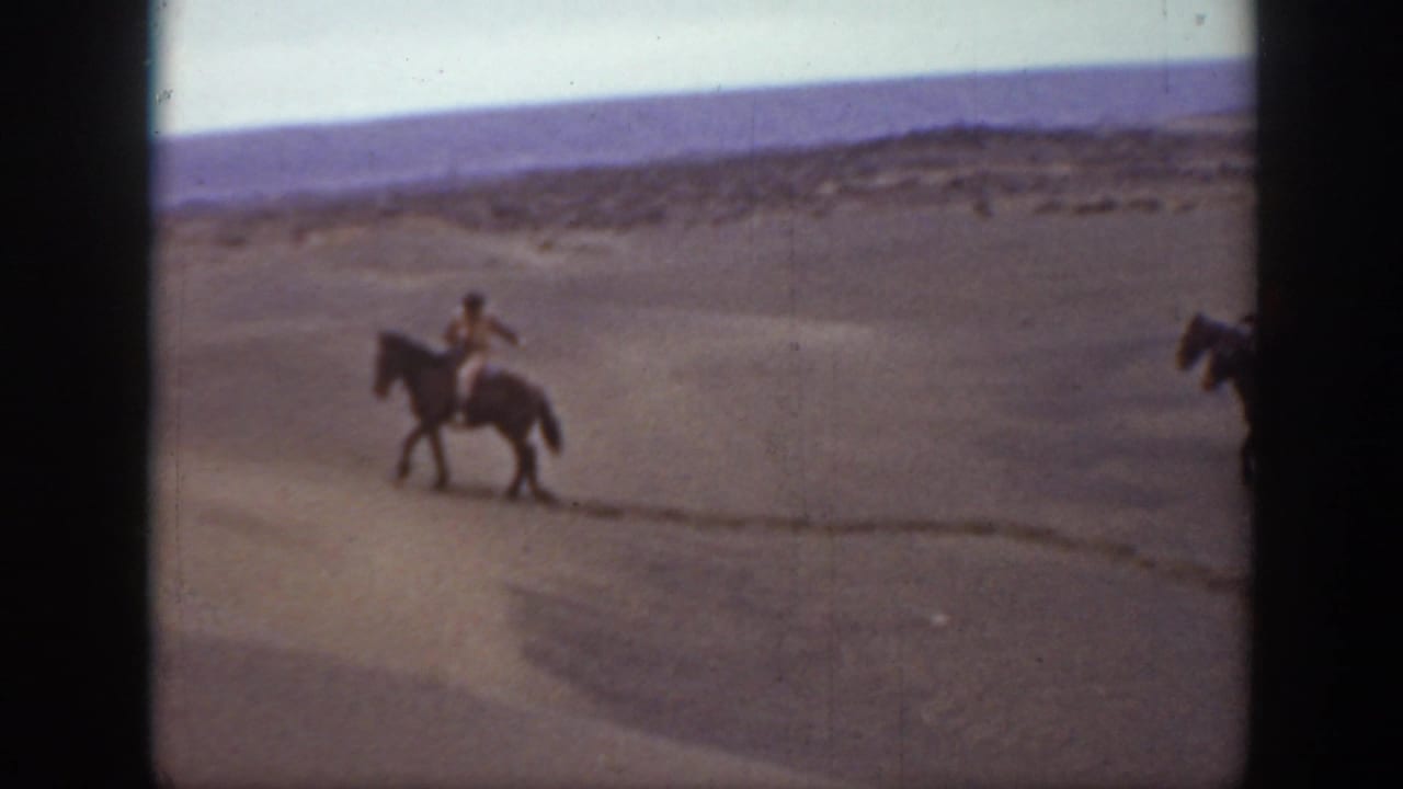 In 1939 Montana home-movie footage, a distant horseback rider moves across an arid landscape with dark film edges visible.