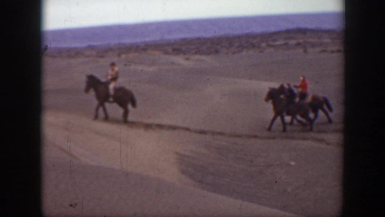 Three riders on horseback appear in the Montana landscape, with one rider ahead and two following across the sandy ground.