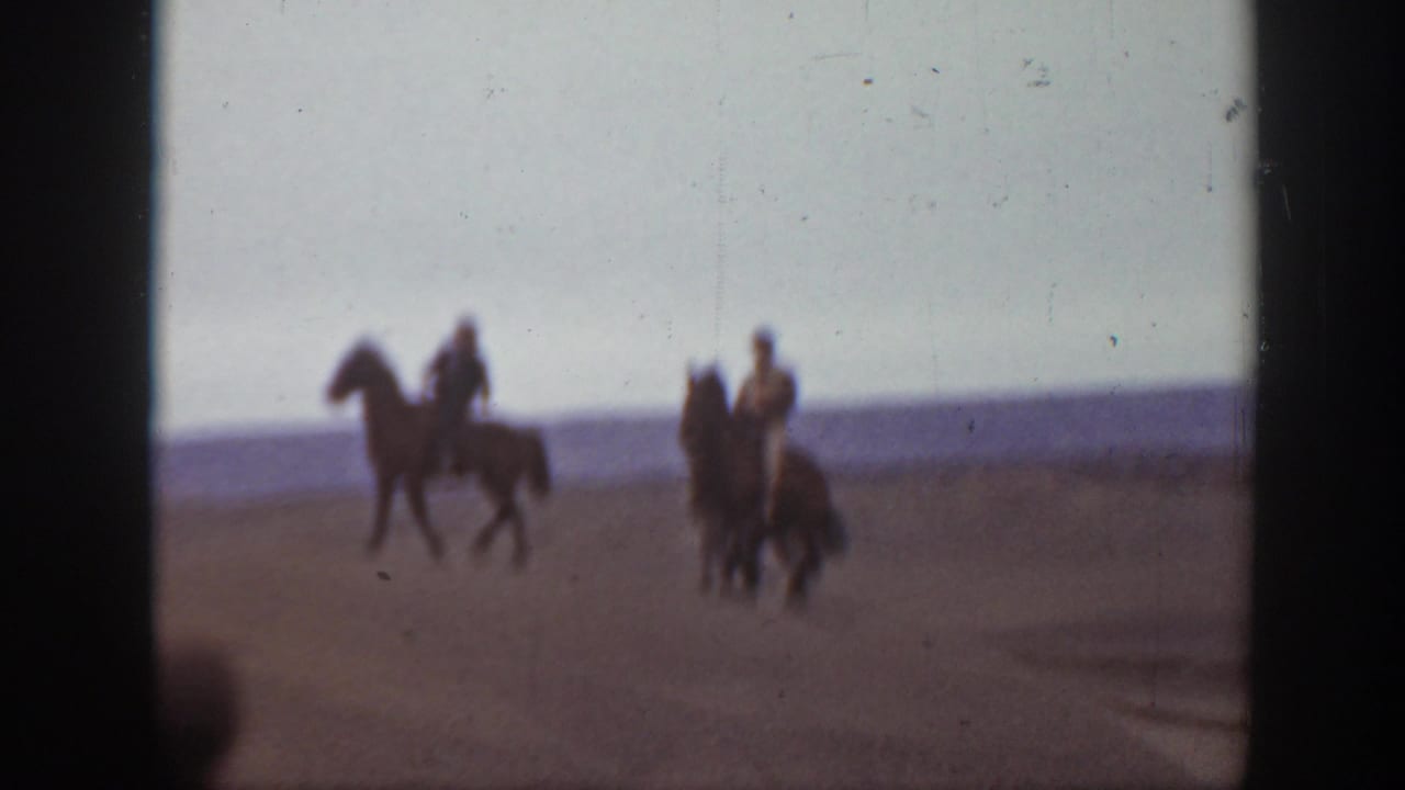 In 1939 Montana home-movie footage, two men on horseback appear in a soft, grainy view of open sand dunes.
