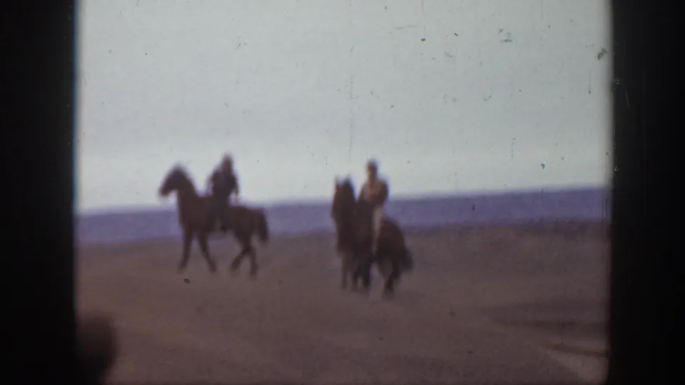 In 1939 Montana home-movie footage, two men on horseback appear in a soft, grainy view of open sand dunes.