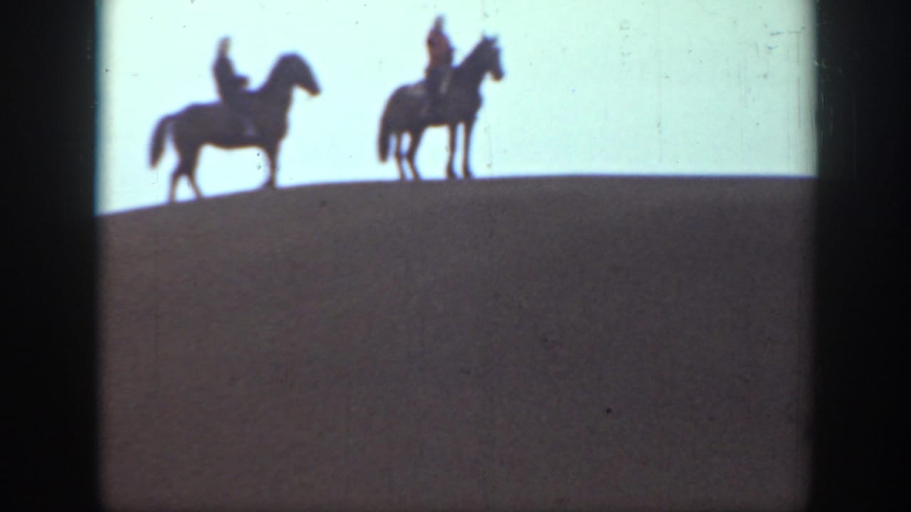 In 1939 Montana home-movie footage, two mounted riders appear in silhouette along a rounded hilltop under a pale sky.