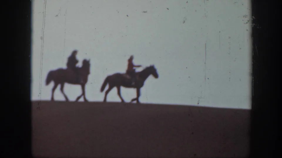 The riders and horses continue along the hill in soft 8mm silhouette, with the sky filling most of the frame.