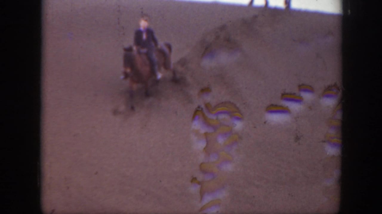 1939 Montana home-movie frame of a rider on a horse in an arid open landscape, with color fading and gate-edge damage visible.