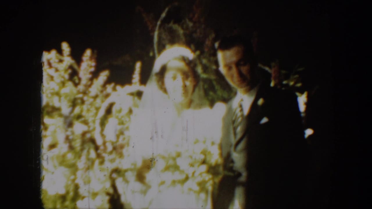 A 1939 Montana home-movie frame shows a bride in a white veil and a groom in a dark suit standing together among flowers.