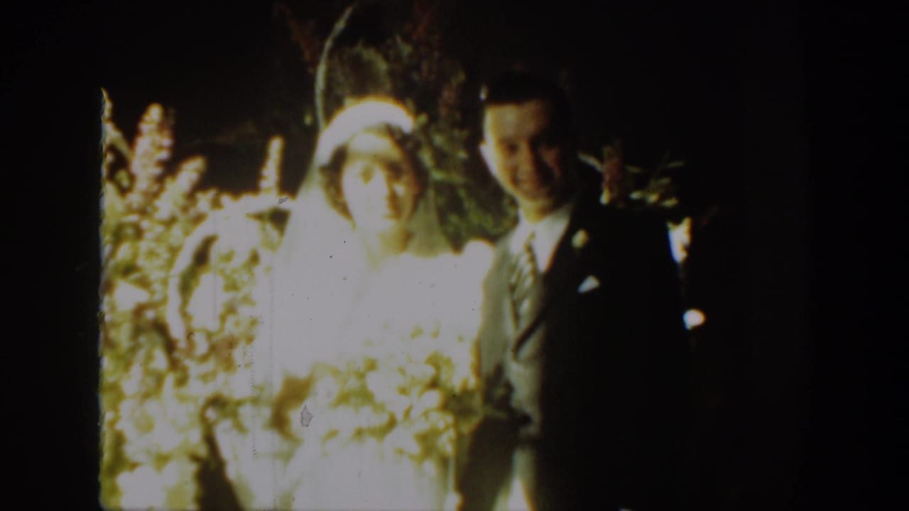 Bride and groom face the camera, framed by flowers and strong warm light.
