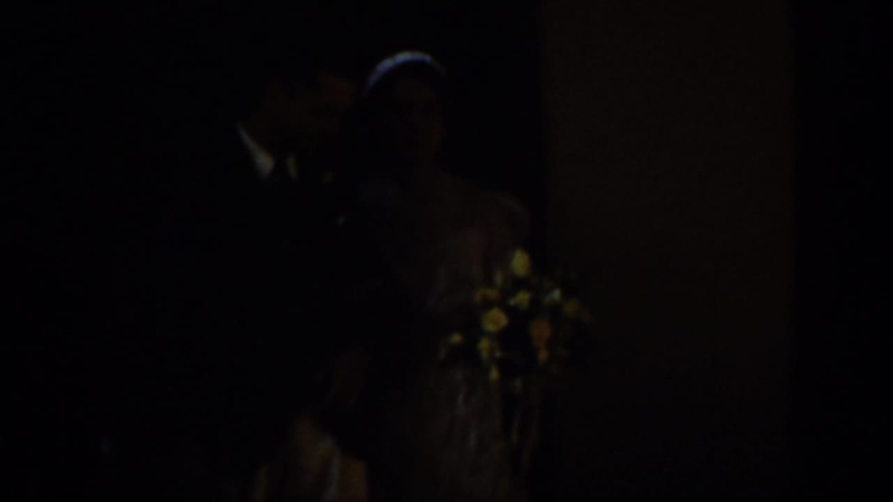 A bride and groom appear in low light during a 1939 Montana wedding home movie, with flowers visible near the couple.