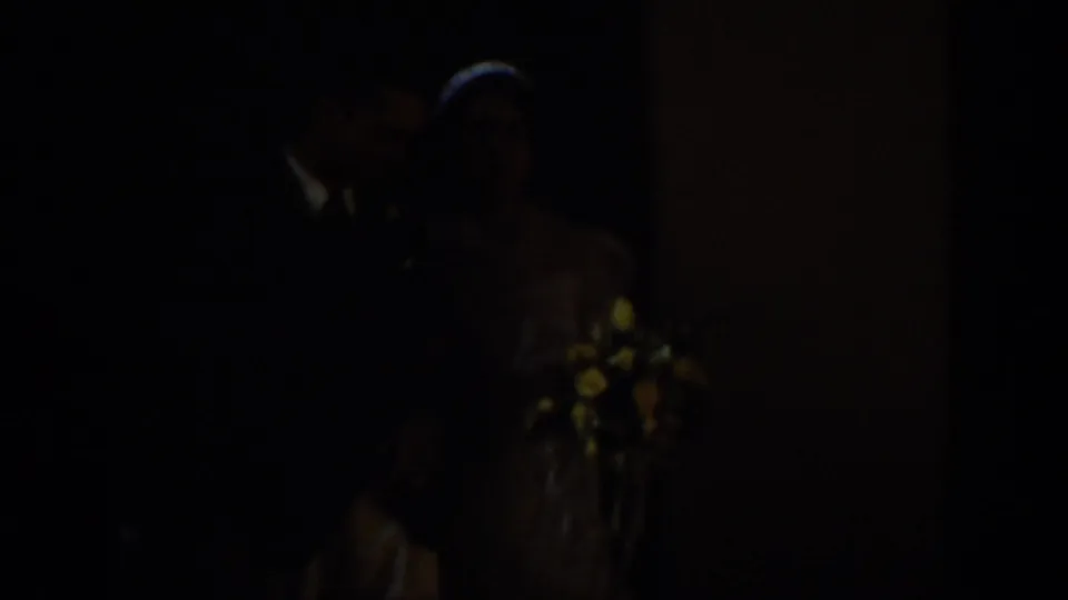 A bride and groom appear in low light during a 1939 Montana wedding home movie, with flowers visible near the couple.