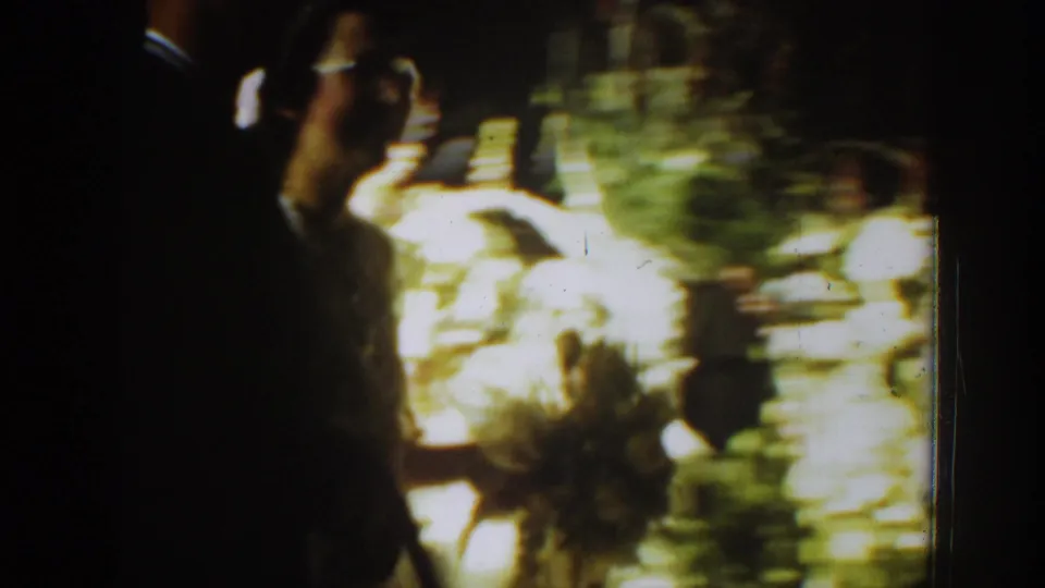 Handheld 8mm frame shows blurred movement near a doorway, with the bride's bouquet and figures passing through the wedding scene.