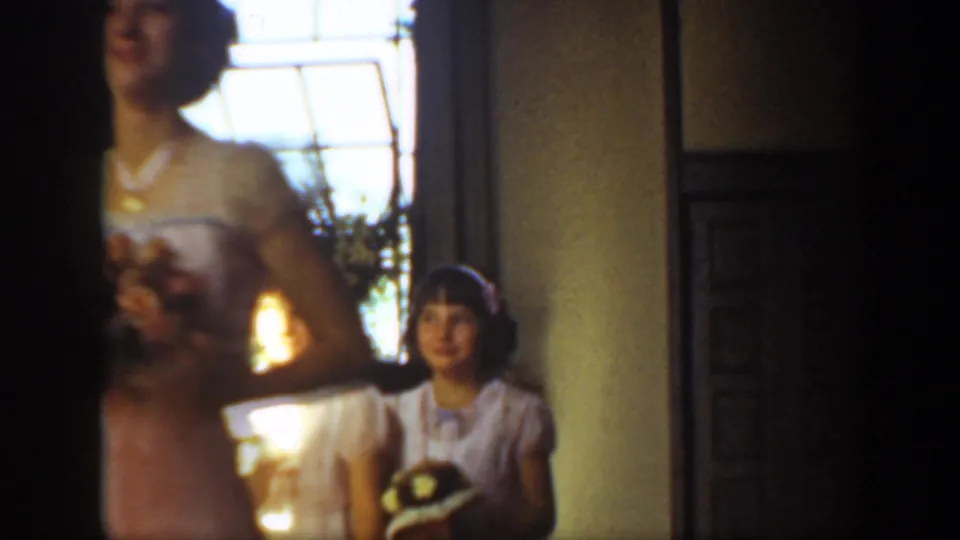 A bridesmaid in a pink dress holds a bouquet while a young attendant stands in the background inside the wedding interior.