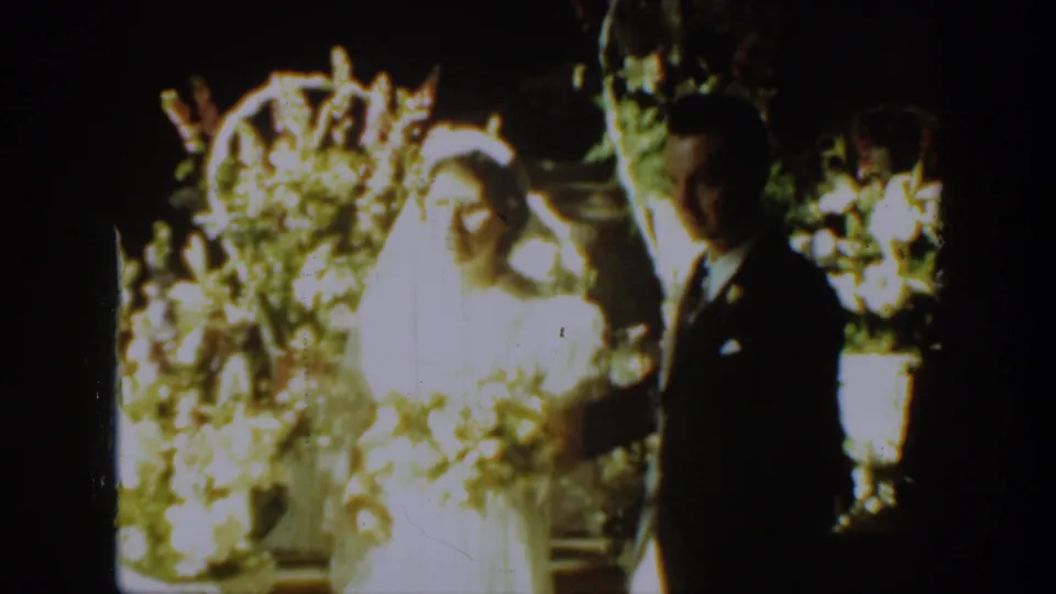 The couple faces the camera in a posed wedding moment, with bright flowers and greenery behind them in Montana, 1939.