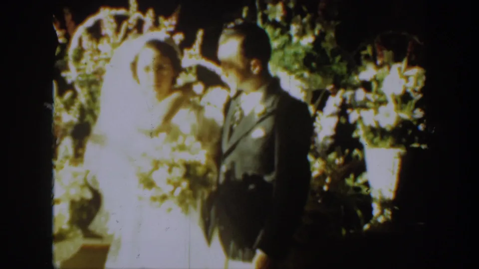 The bride and groom appear turned toward one another beside bright flowers in this 1939 Montana wedding footage.
