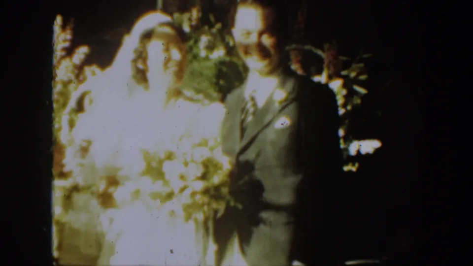 1939 Montana 8mm frame of the bride and groom smiling together, with bright flowers and a bouquet visible.