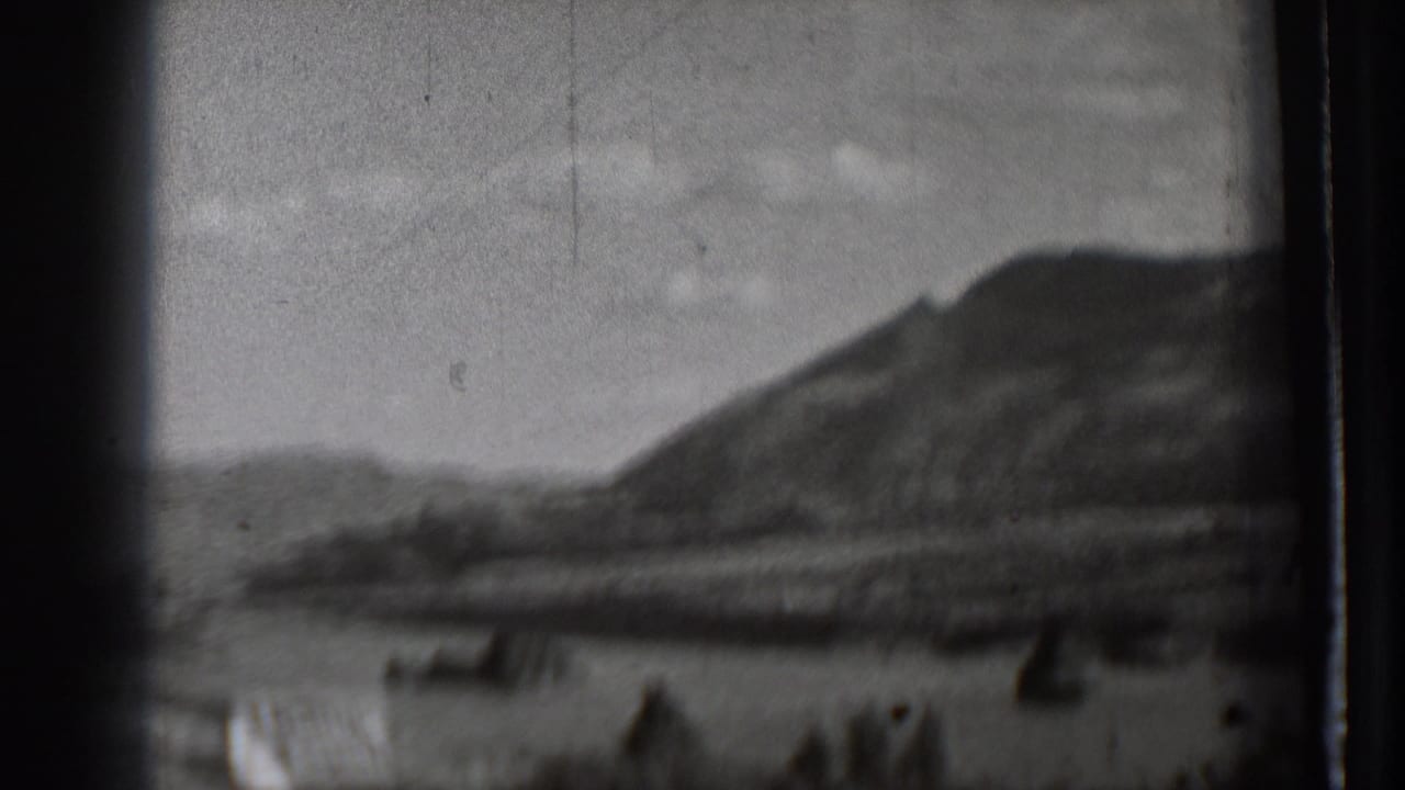 Soft black-and-white mountain landscape across water with dark shapes near the shoreline.