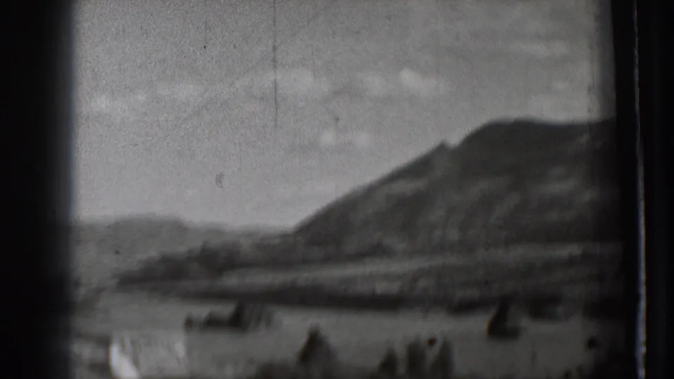 1939 Washington 8mm frame showing a blurred mountain slope beyond water, with small dark shapes near the shore and heavy film-edge shadowing.