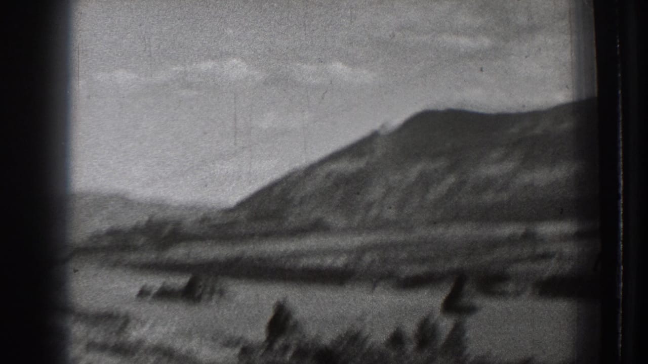 Black-and-white 8mm view of a Washington mountain lake scene, with blurred dark forms near the waterline and visible dust and scratches.