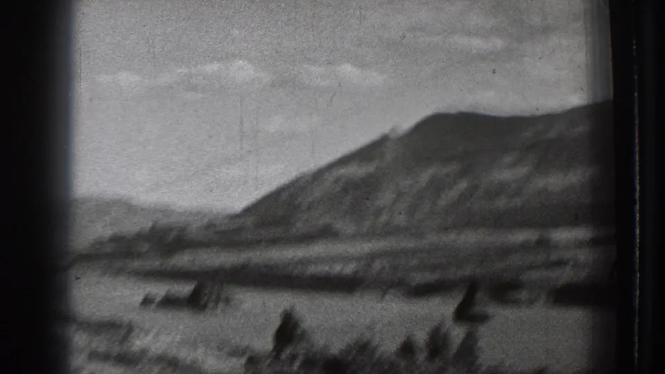 Black-and-white 8mm view of a Washington mountain lake scene, with blurred dark forms near the waterline and visible dust and scratches.