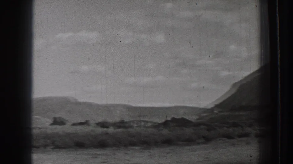 1939 Washington 8mm frame showing arid shoreline terrain, low mountains, scattered rocks, and a cloudy sky from a moving viewpoint.