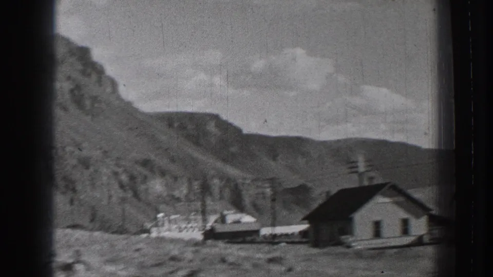 1939 Washington 8mm frame showing a small building, utility poles, and rocky mountain slope in a sparse rural landscape.