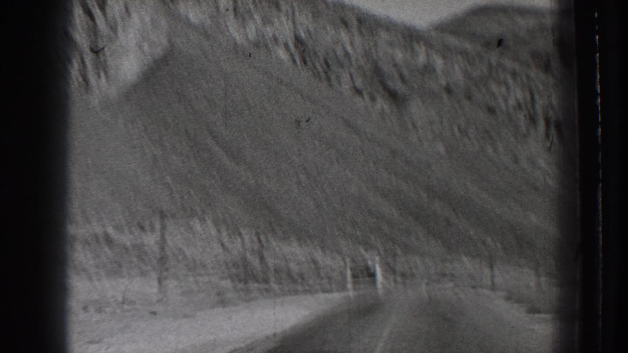 Curving road seen from inside a moving vehicle, with steep hills and dark film borders.