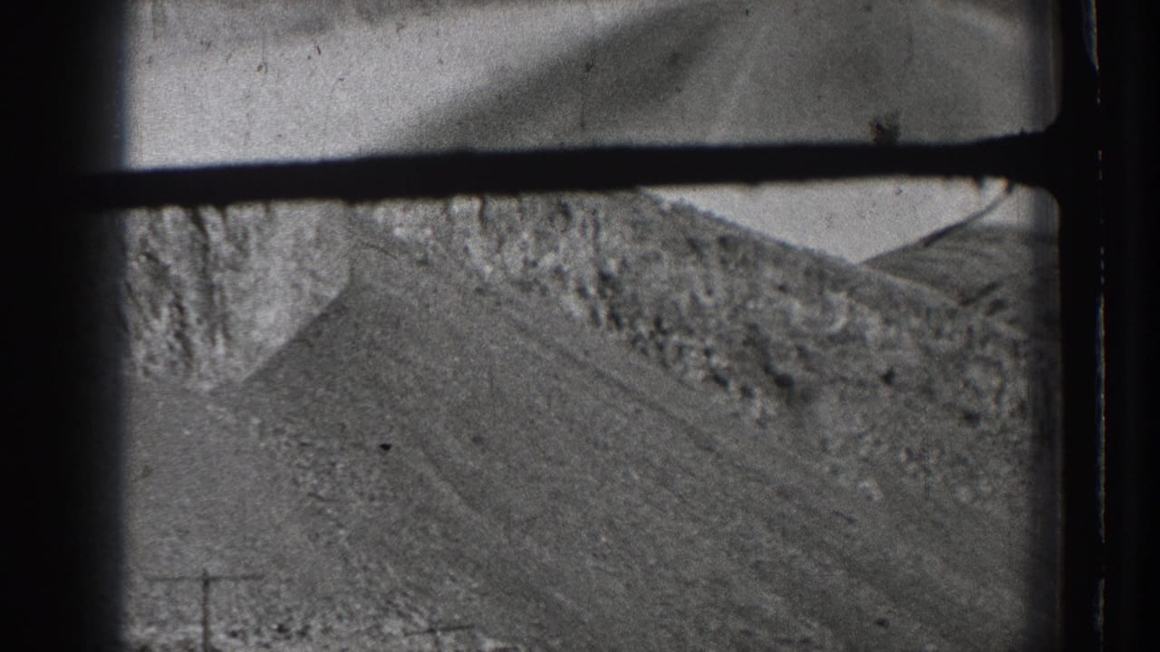 Black-and-white 8mm frame showing a rocky Washington hillside beside a road corridor during a moving-car view.