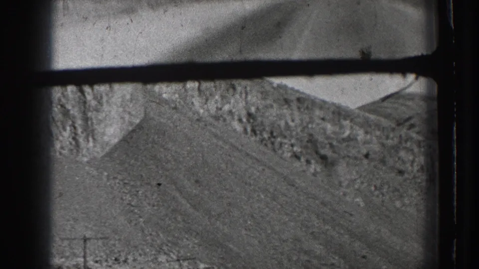 Black-and-white 8mm frame showing a rocky Washington hillside beside a road corridor during a moving-car view.