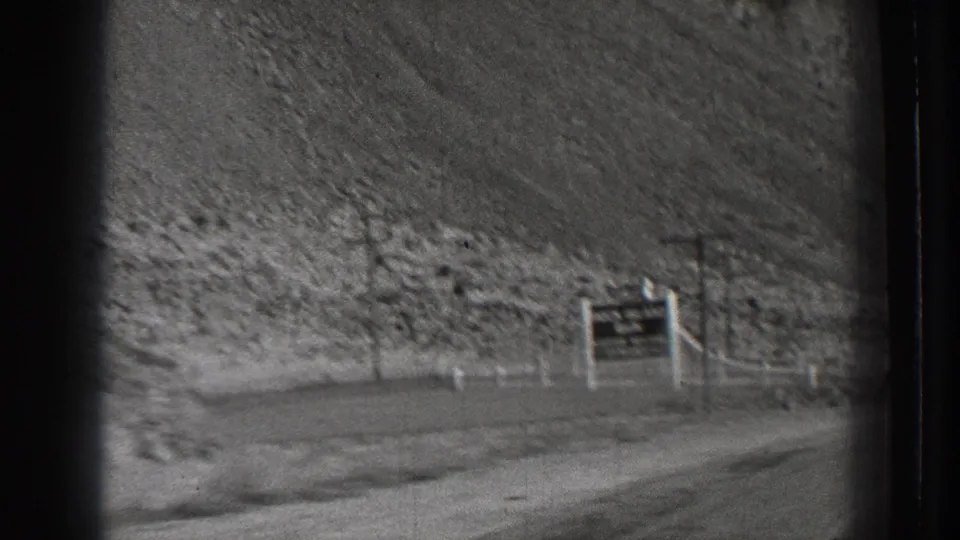 1939 Washington road-trip frame with a brief roadside sign, utility poles, and a steep rocky hill beyond the road.