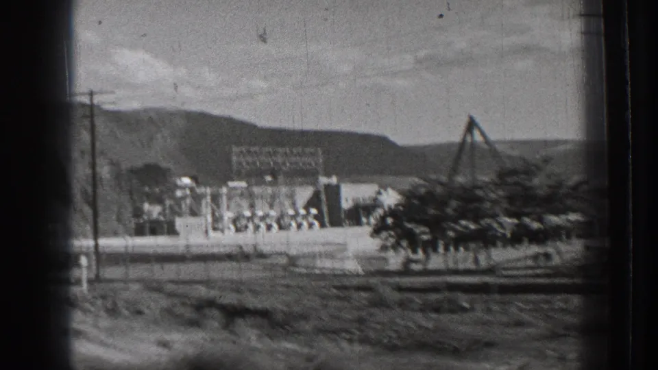 1939 Washington moving-vehicle view appears to show Rock Island Dam structures, utility poles, a sloped support, and surrounding hills.