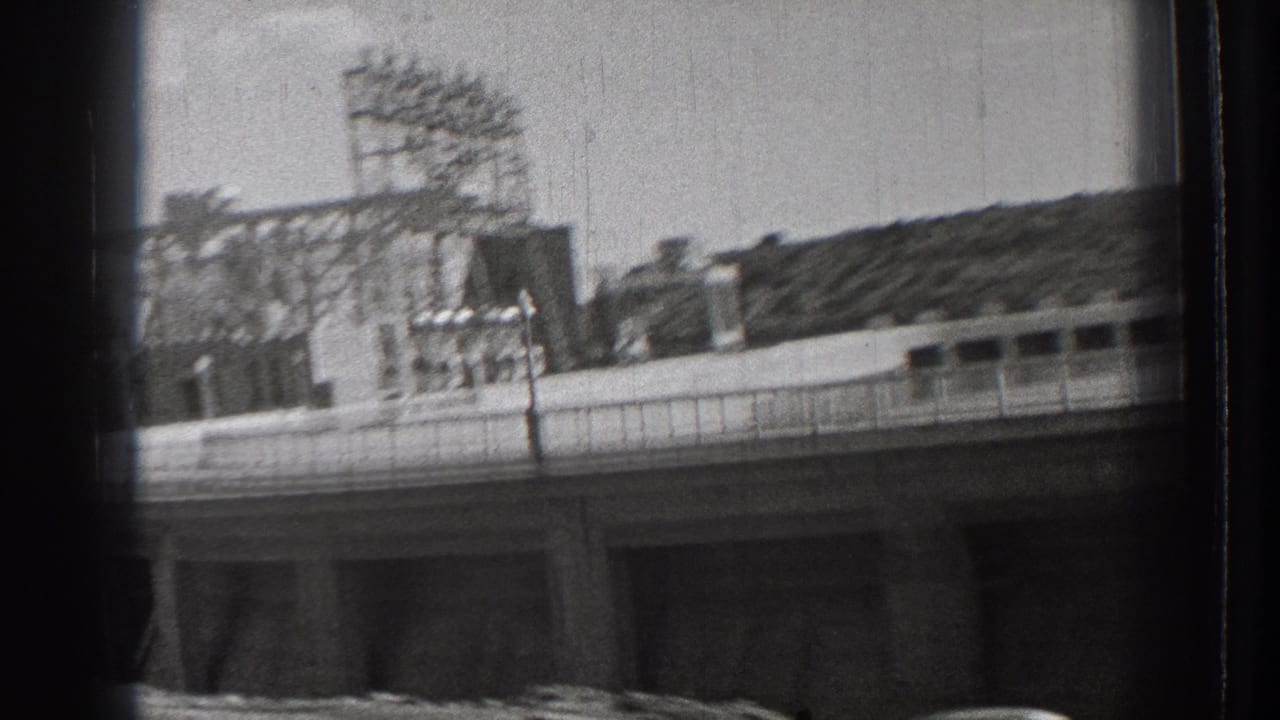 Concrete dam or bridge approach with railing, power-line structure, water, and hillside beyond.